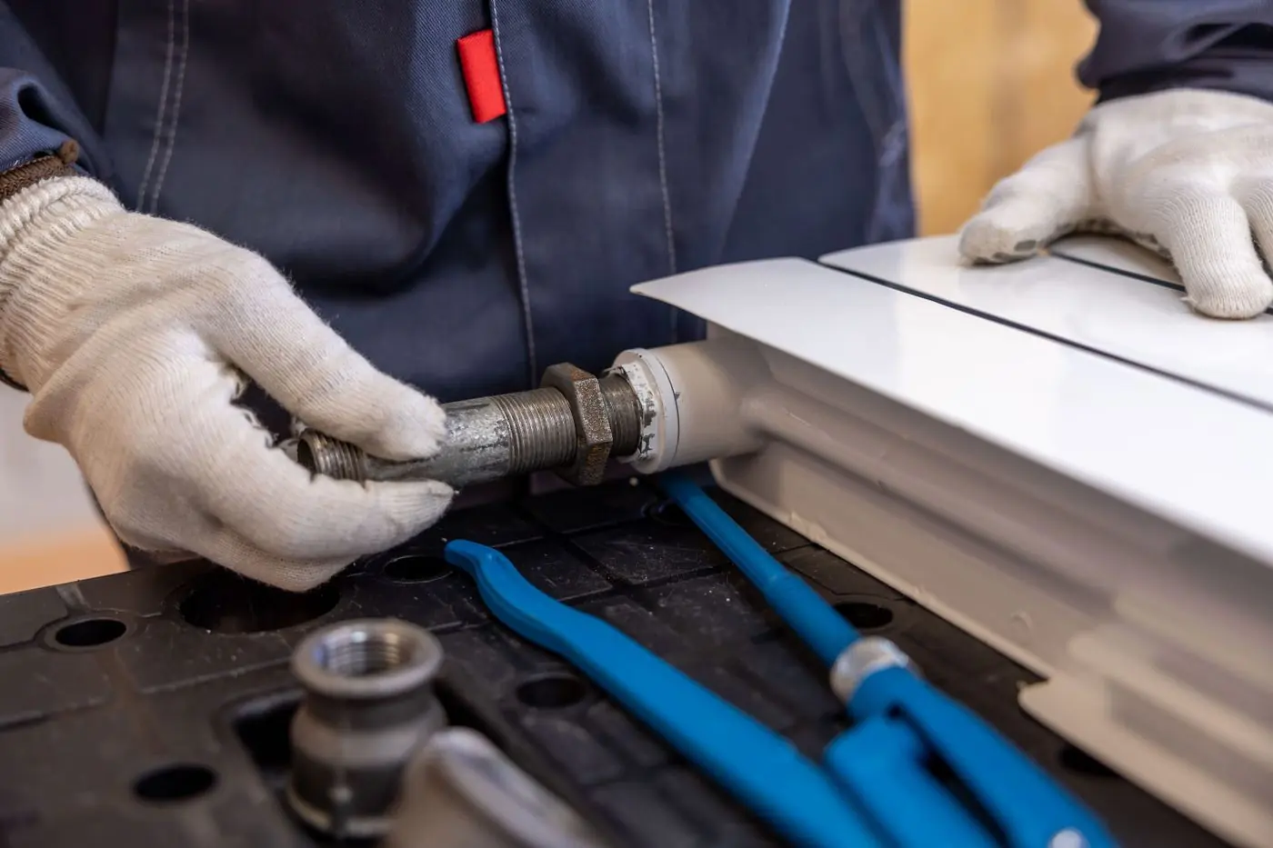 Handen met handschoenen monteren een leiding aan een radiator
